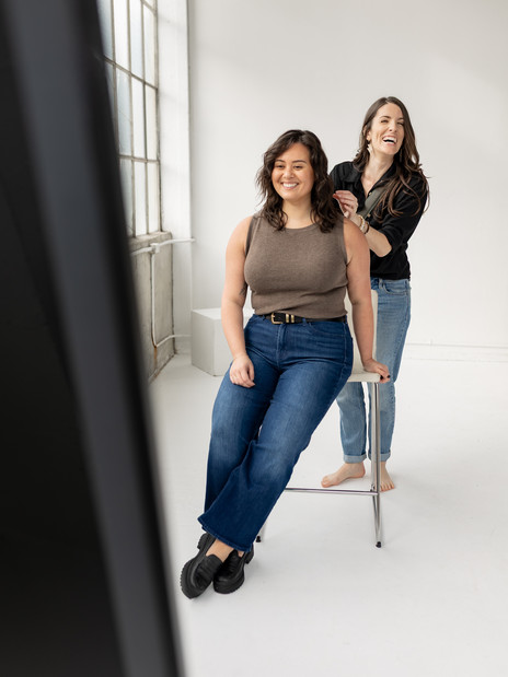 Brand photographer showing client how to pose on stool in front of mirror at Seattle studio.