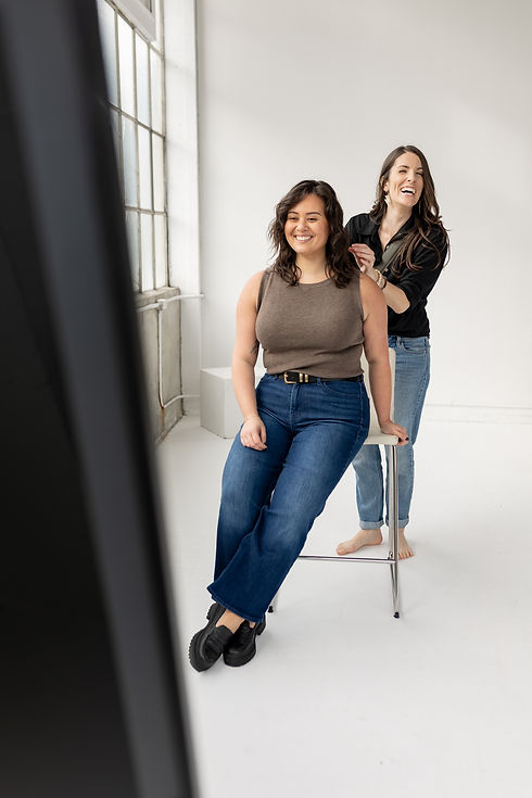Brand photographer standing behind client, guiding them how to pose in photography studio.