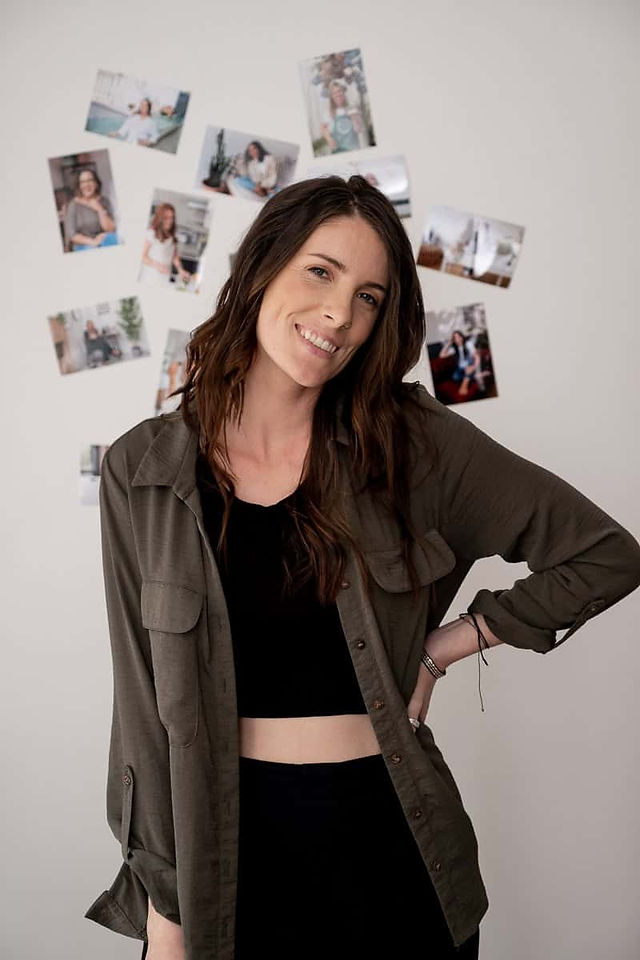 Smiling professional brand photographer in casual outfit standing in front of photo wall during branding photoshoot in New Brighton Photography studio.