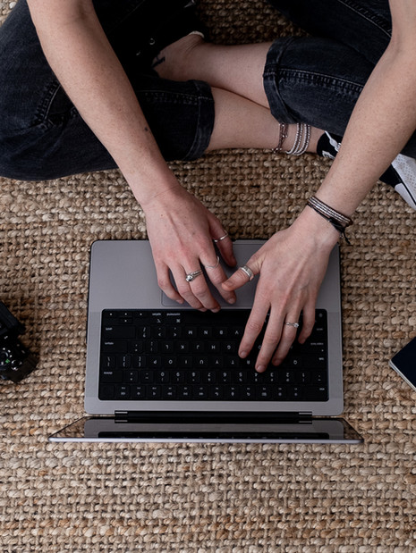 Overhead image of photographer with rings on fingers, typing on laptop.