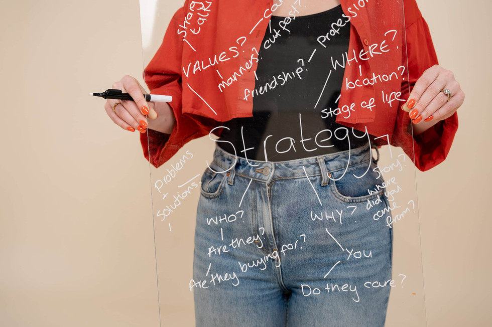 Web designer writes brand strategy keywords on a transparent board, wearing a red jacket.