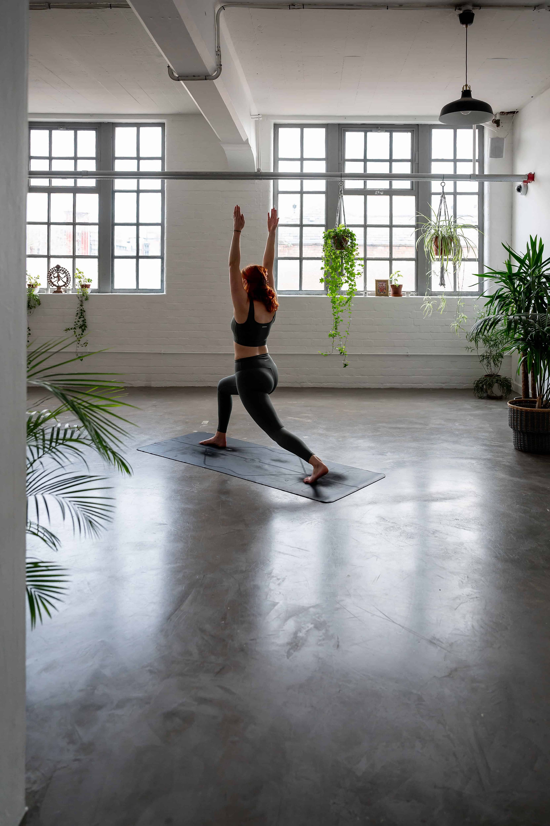 A person is performing a yoga pose on a mat in a spacious, well-lit studio with plants and large windows, captured beautifully by Wild Kind Photography.