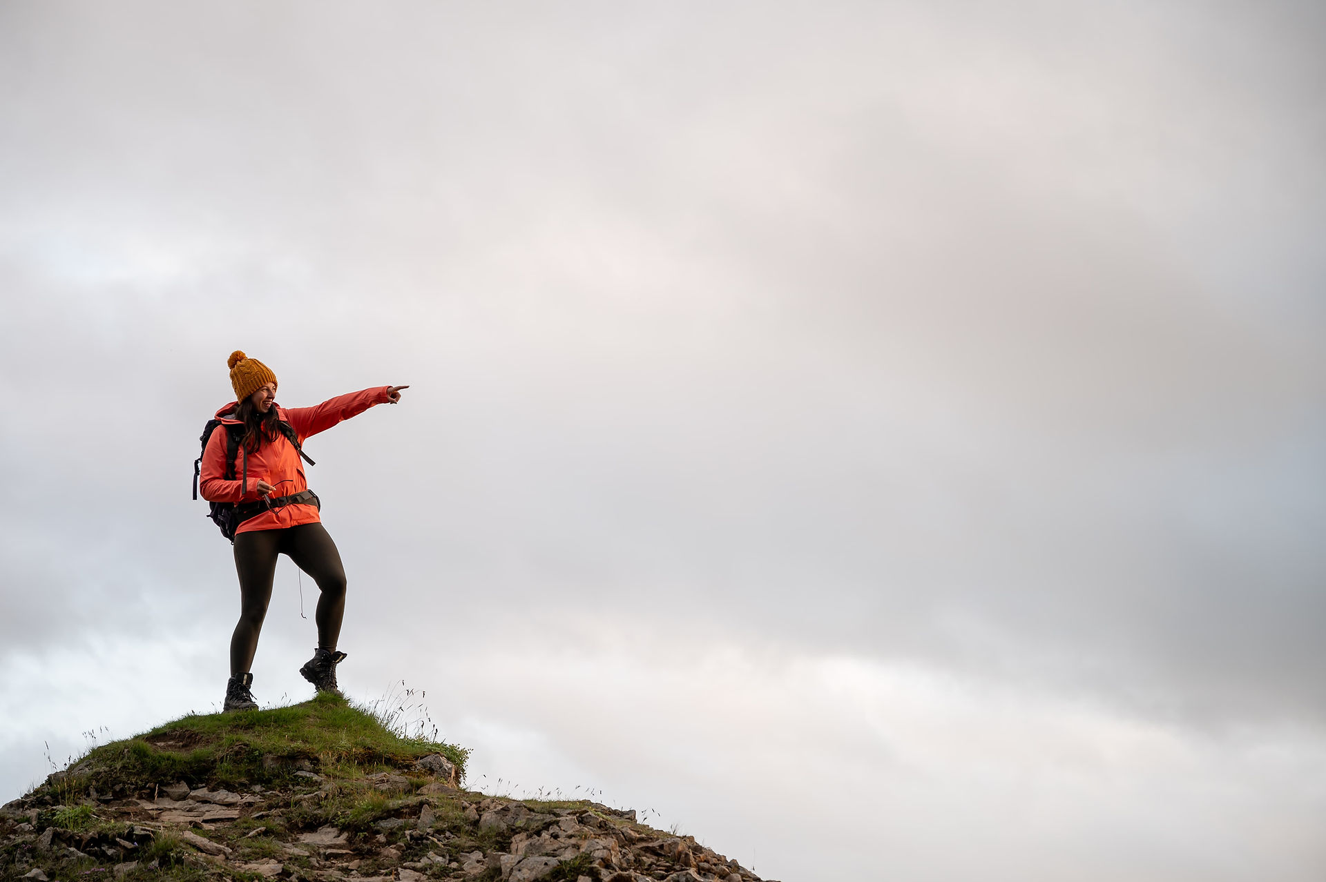 Lady is stood on top of hilly, mountain. pointing into the distant.