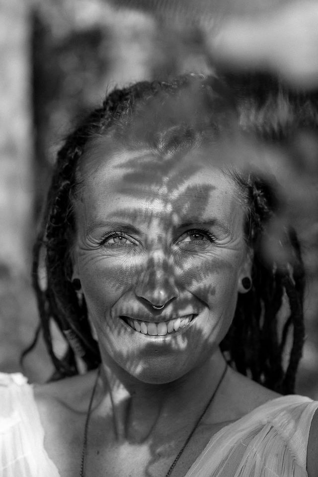 Black and white portrait from a brand photoshoot abroad, featuring a smiling woman with dreadlocks, fern shadows crossing her face.