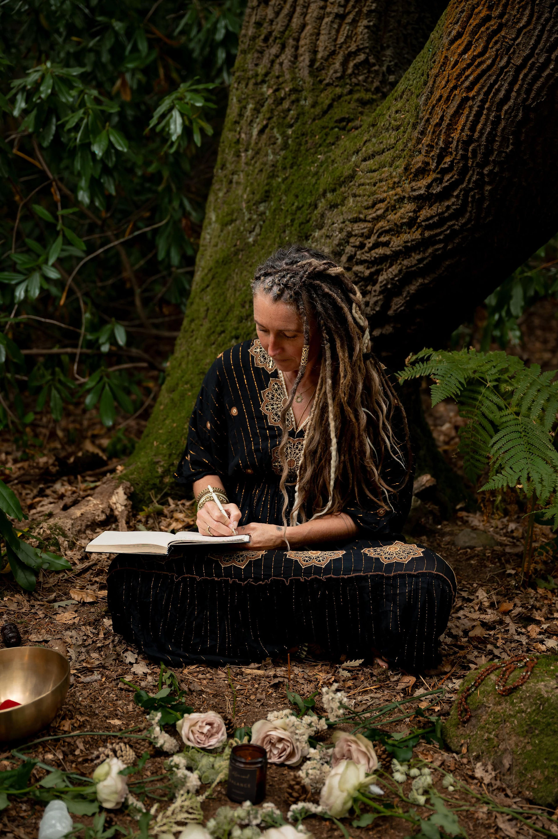 Chloe Ward writing in a notebook on a tree stump, surrounded by greenery during her Wirral-based brand photoshoot.