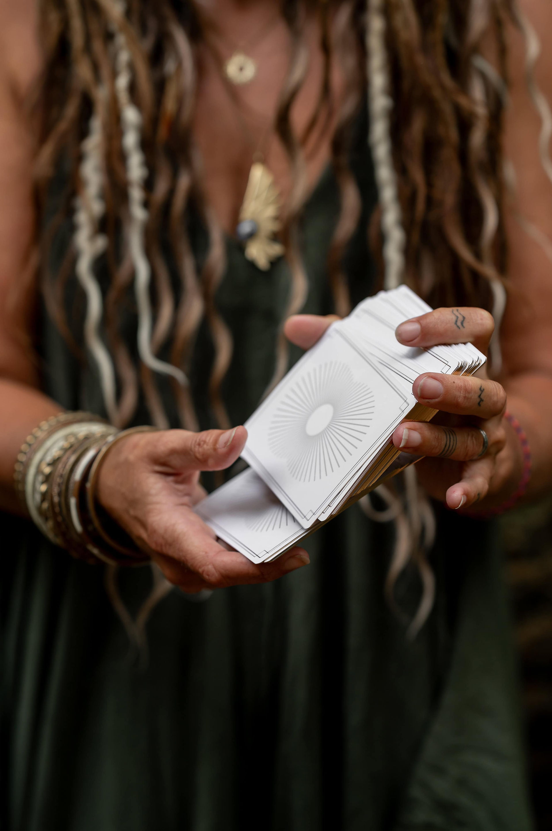Close-up of hands holding a deck of oracle cards, with rings and bracelets.