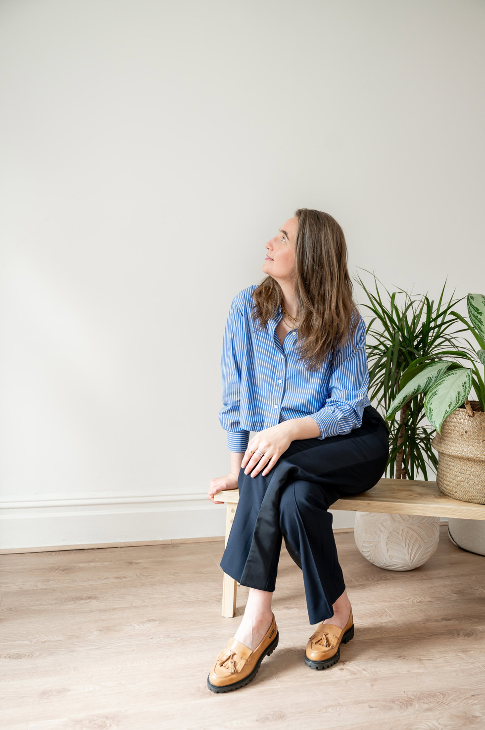 Therapist in blue shirt sitting on bench in New Brighton photography studio, looking up at blank wall.