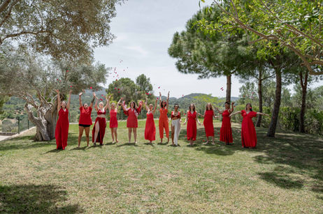 Group of women in red dresses throwing red rose pedals into the air at goddess retreat in Majorca.