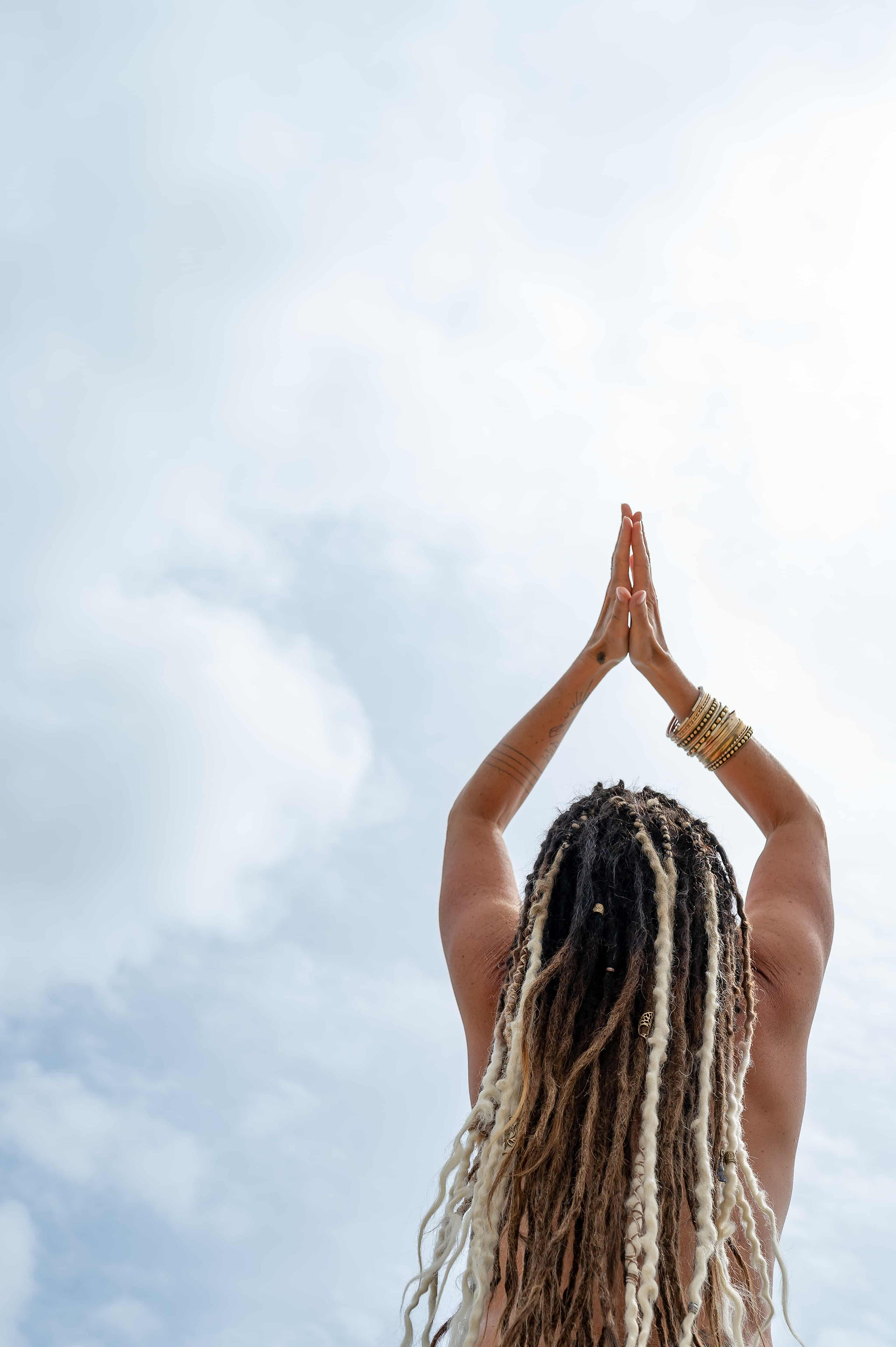 Yogi holding hands above head in prayer pose facing away from camera, topless.
