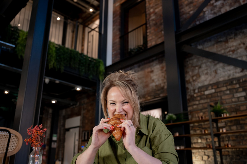 Rachael Does Design eats croissant and laughs outside a modern industrial café space.