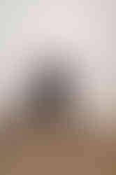 Web designer sits barefoot on a wooden chair in a relaxed studio pose, smiling confidently.