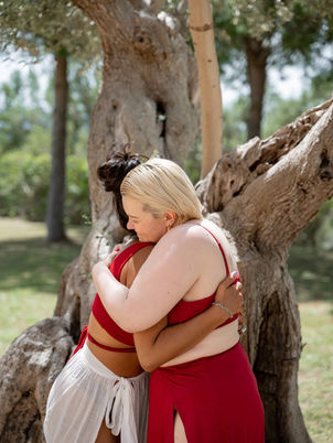 Two women in red dresses hugging after goddess retreat in Mallorca.