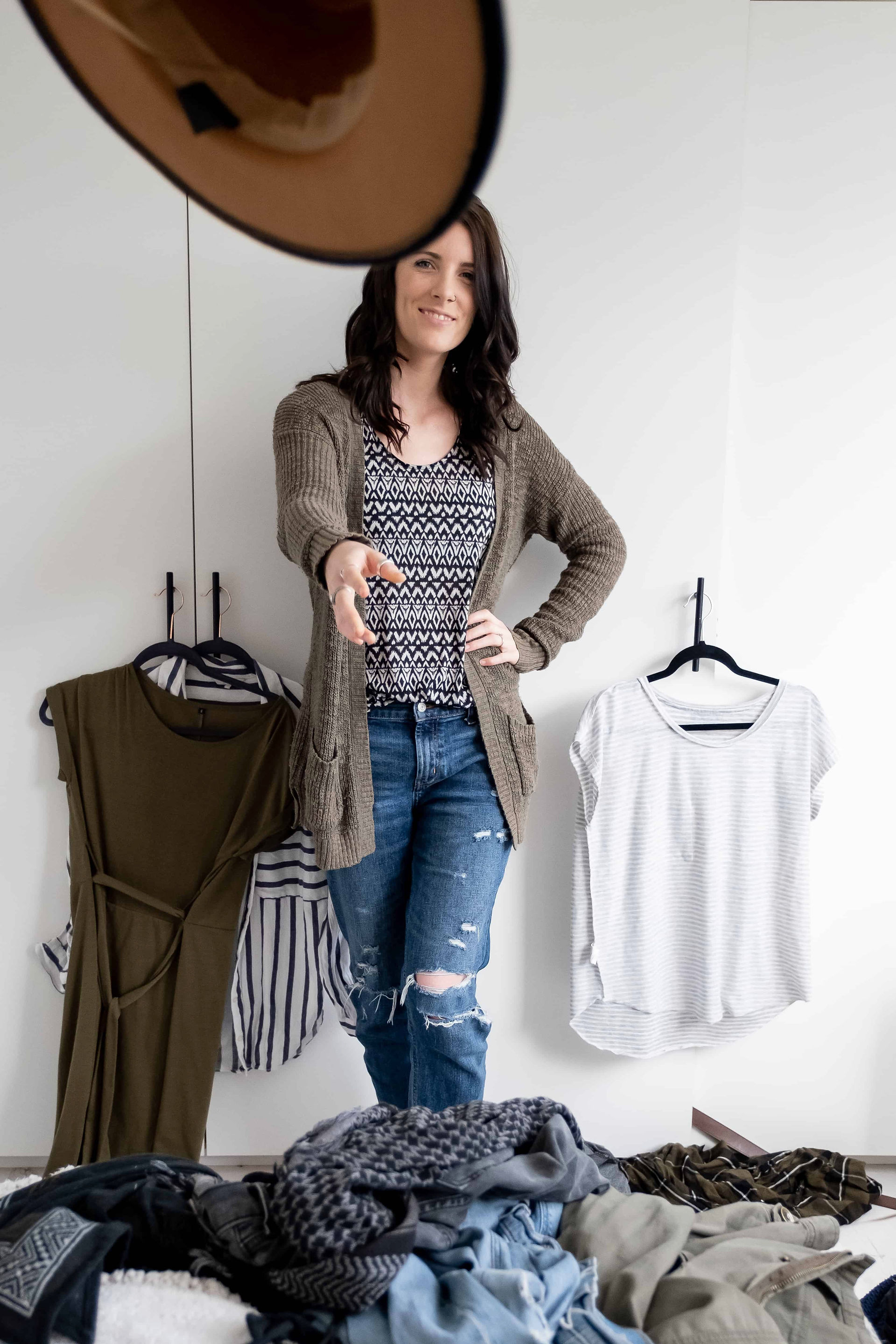 Brand photographer throwing hat at camera with clothes piles around her.