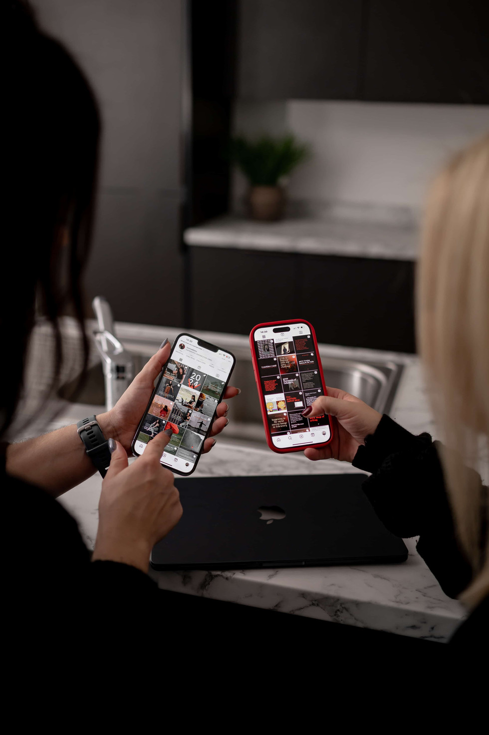 Two women having a personal brand photoshoot in a kitchen, comparing instagram accounts.