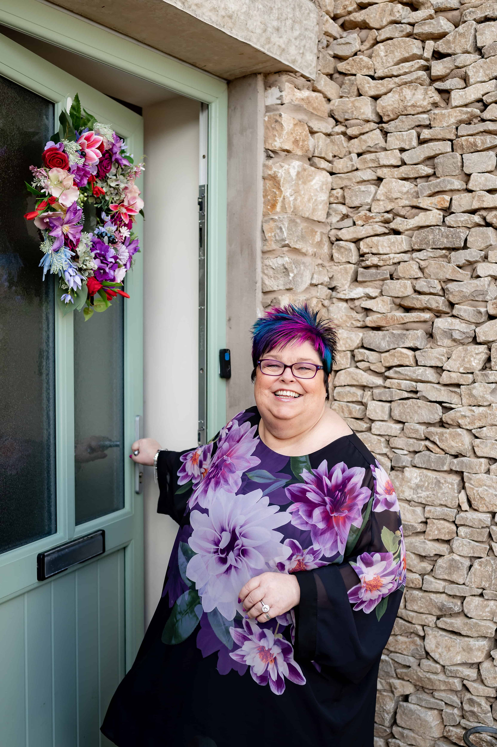 A woman standing in front of a stone house with a flower wreath during Lancashire Brand Shoot
