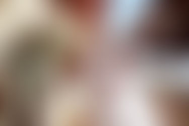 Six diverse people form a circle with their fists, smiling and wearing colorful sweaters. The sky and brick wall are visible in the background.