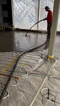 Construction worker smoothing concrete floor with hose, white tubing. Underfloor Heating installation underway