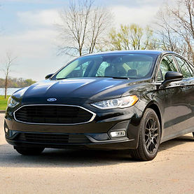 Black Ford sedan parked on pavement near green grass and trees