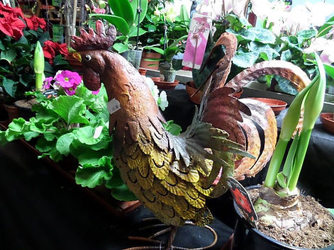Decorative metal rooster statue among potted garden plants