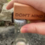 Thumbnail: A bottle opener engraved to say "DON'T MIND IF I BREW!" with a maple handle and a bent nail on the end to remove bottle caps being shown in the process of removing a cap off a bottle of hard cider