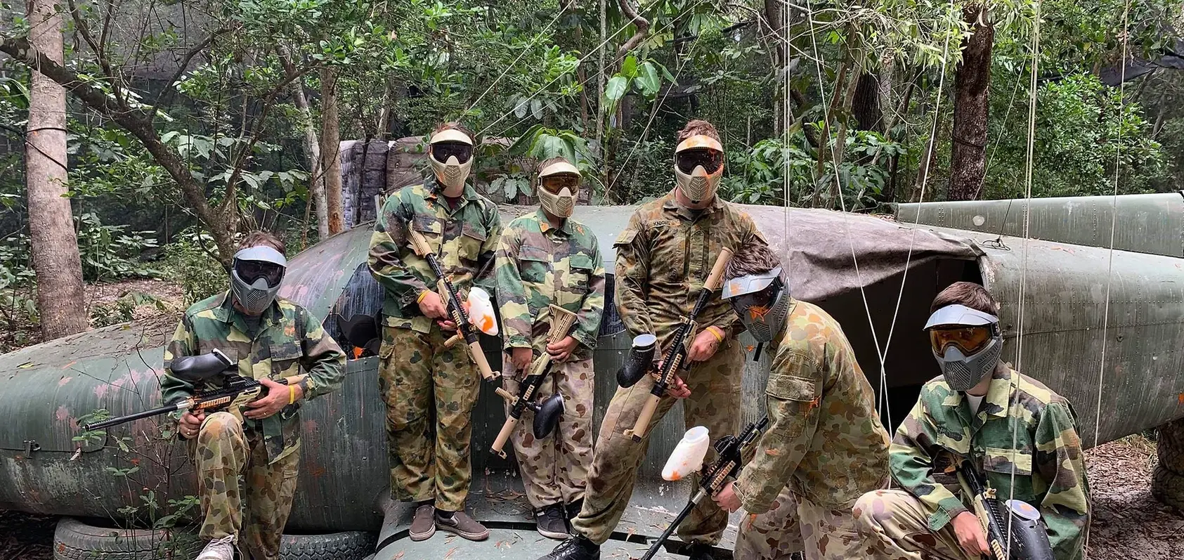 6 people in camo gear with paintball equipment posing on aircraft carcass at Xperiences HQ at Sunshine Coast