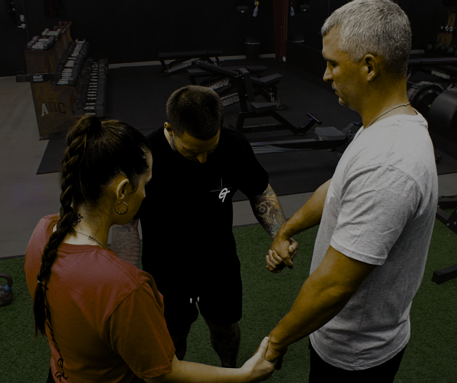 two men and one woman holding hands in a circle with their heads bowed to pray.