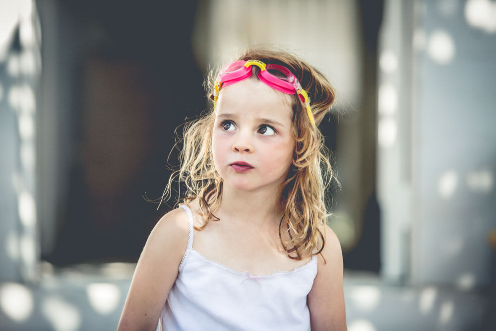 Young girl with goggles on her hear looking up and away from the cameraduring a Day - In - The - Life photography session. Suzanne Stevenson Photography Sydney