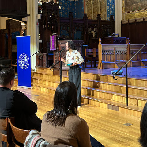 Woman sharing in front of audience. CT State Community College banner on the side.