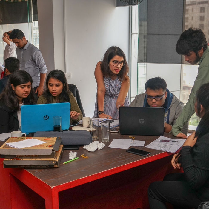 Five diverse team members collaborating on laptops at a modern office desk.