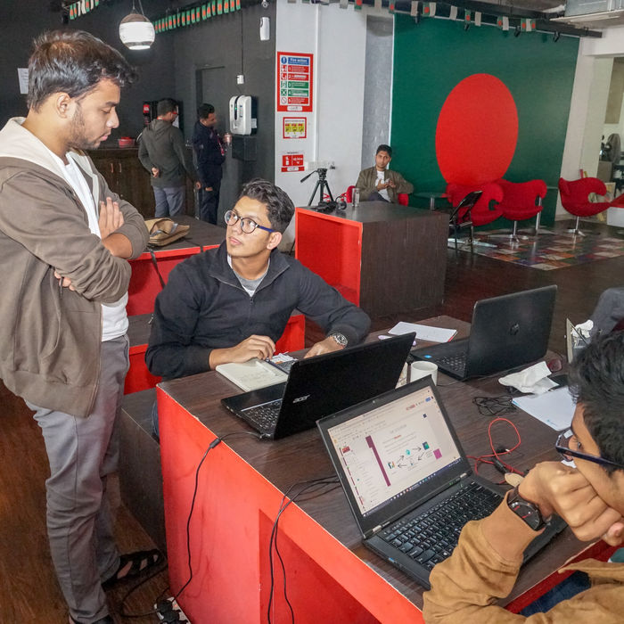 Three young men collaborate, discussing work around laptops in office.
