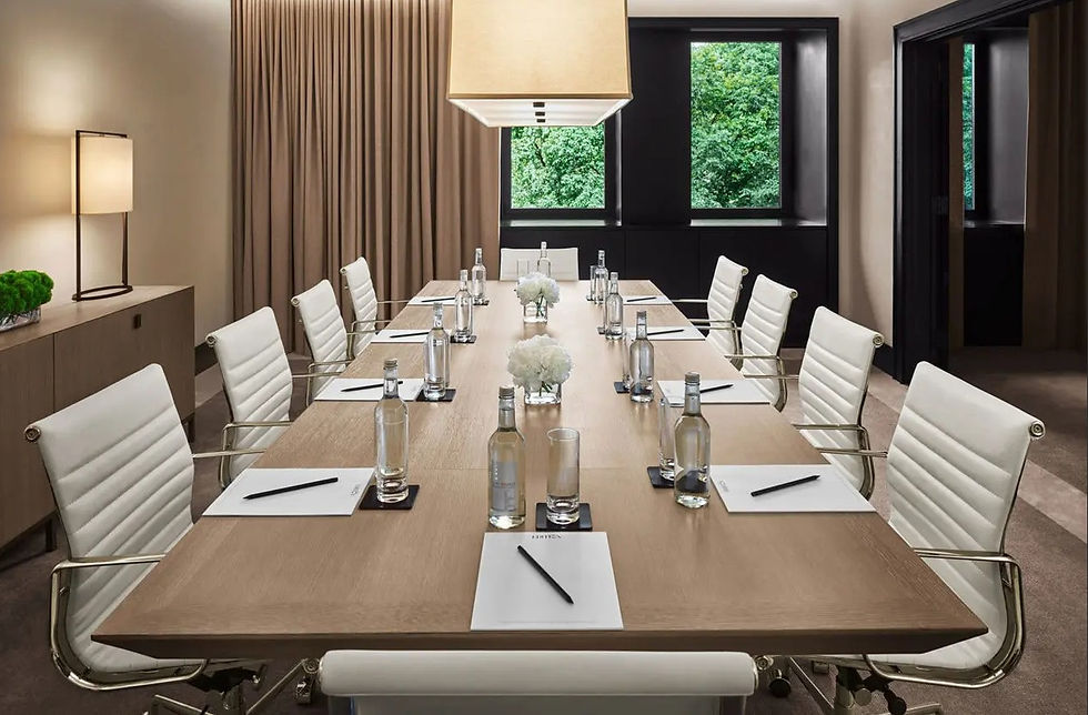 Meeting room with wooden table, white chairs, notepads, and natural light from a window overlooking greenery.