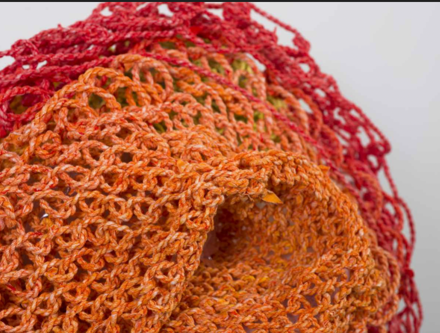 Image of handmade paper netting in orange to red gradient blossoming into a round shape.