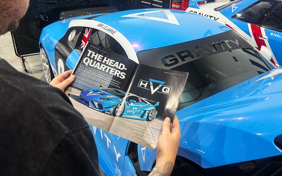 man holding open the gravity annual with a blue Audi R8 in the background