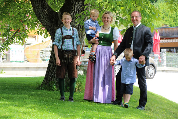 Lächelnde Familie in Tracht unter einem grünen Baum.