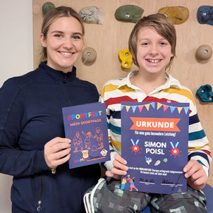 Ein Junge sitzt und hält seine Urkunde neben seinem Therapeuten