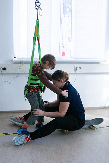 Ein Kind in der Physiotherapie mit Sicherheitsgurten zur Unterstützung beim Gehen