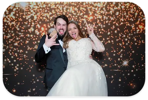 Happy bride and groom making rock gestures on a glittery background