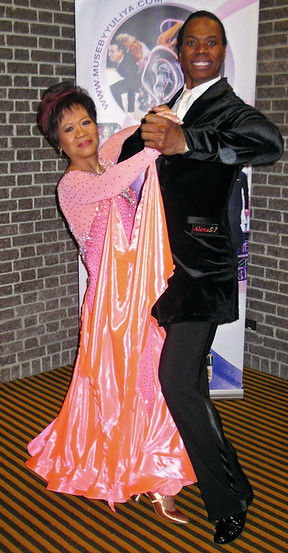 A smiling couple in elegant dance attire is captured in a Tango pose.