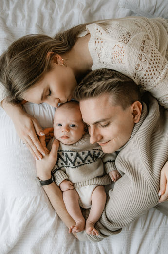New parents lying on the bed with their newborn, sharing a quiet bonding moment during an in-home lifestyle session.