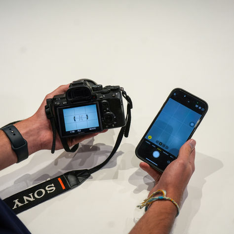 Two hands holding a camera and a phone, both on with the camera view pulled up on the screen.