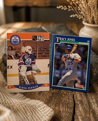 A sports card display featuring a Pro Set hockey card of Edmonton Oilers goaltender Eldon Reddick alongside a 1991 Score baseball card of Tracy Jones of the Mariners, resting on a rustic wooden surface with a slate piece and a vase of dried grass in the background.