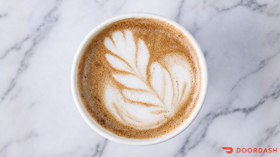 An overhead view of a coffee topped with leaf-shaped latte art on a white marble-patterned counter.