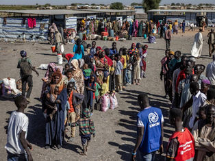 Sudanese refugees gathered in a crowded camp in Chad, with makeshift shelters and humanitarian aid workers distributing supplies.