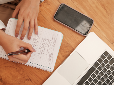 Woman writing marketing strategy notes in a notebook beside a laptop and smartphone on a wooden desk – small business planning concept.