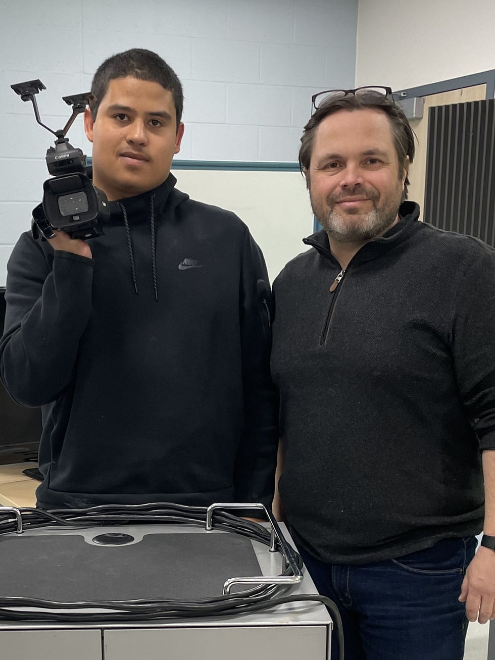 Two men standing next to one another. One is holding a video camera.