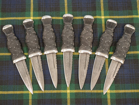 Set of 7 matching traditional Scottish Sgian Dubhs with carved Bog Oak handles, Dundee Agate pommel stones, Sterling Silver fittings and patterned steel blades.