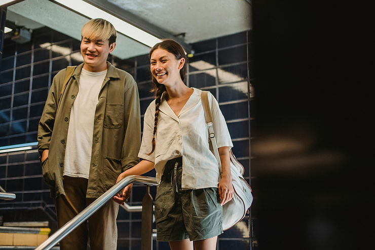 Two friends smiling and holding hands while walking down subway stairs with blue tiled walls. Casual attire, relaxed and happy mood.