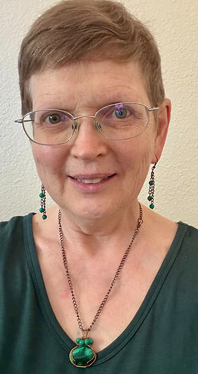 Picture of middle-aged Caucasian woman in green dress and jewelry with glasses. This is Lisa Sonin Larsen, PsyD