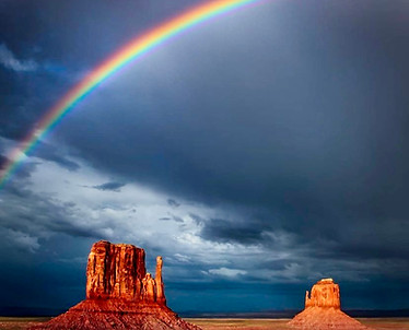 desert scene with rainbow across dark blue clouds