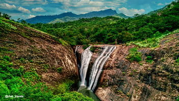 Scenic waterfall cascading down a rocky cliff with lush green forest background.